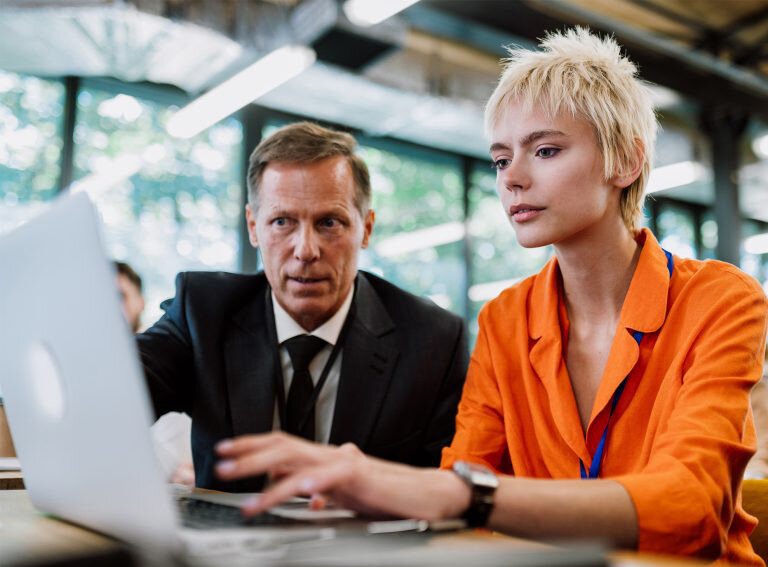 Older man educating younger woman on the computer